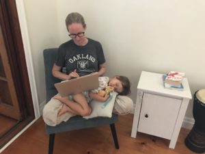 Kelly Matthews writing on laptop, which sits atop her sleeping daughter.