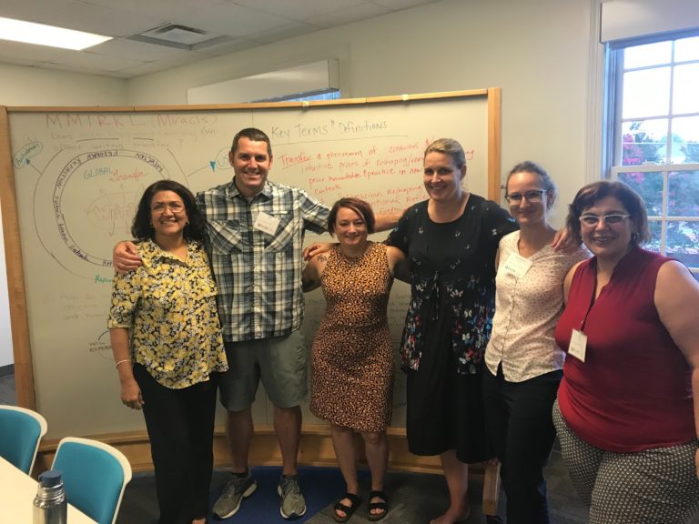This is a group photo of the CEL scholars in this team collaborating together. They are all standing together in front of a white board.