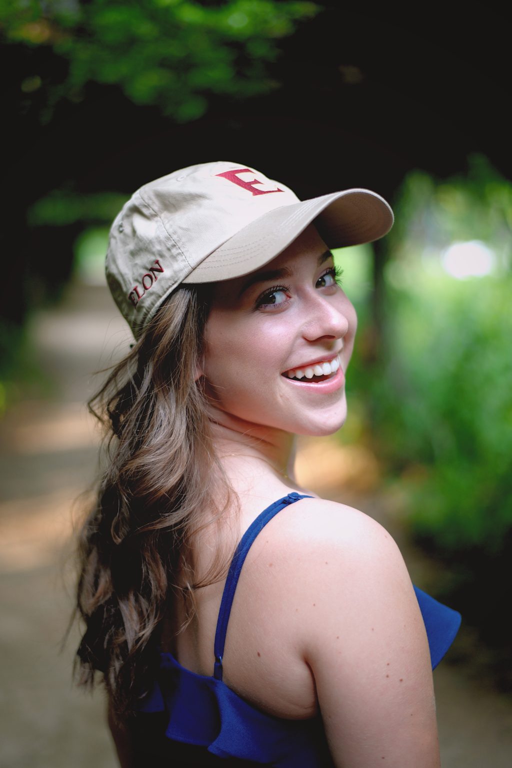 Young woman wearing an Elon baseball cap looking back over her shoulder