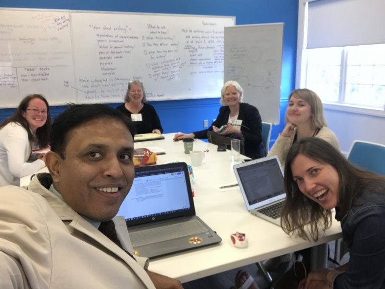 Team Recursivities Group Photo. In this picture, the different global scholars and researchers from around the world are meeting together around a table and in front of a busy whiteboard.