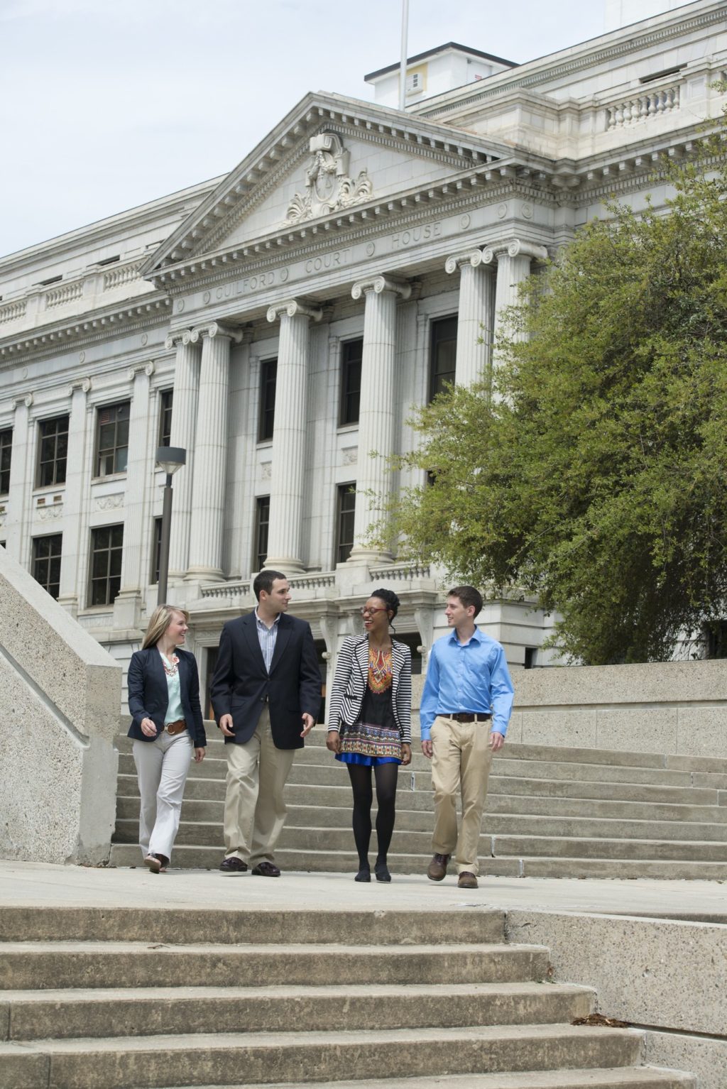 Four students walk down the stairs in front of the Guilford County court house.