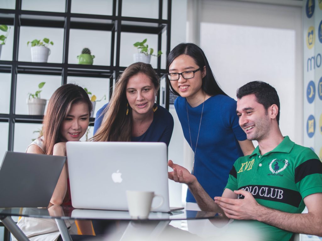 A group of four people look together at a MacBook computer.