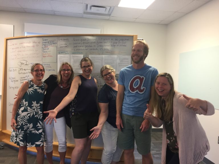 6 people standing in front of a white board, posing for the camera.