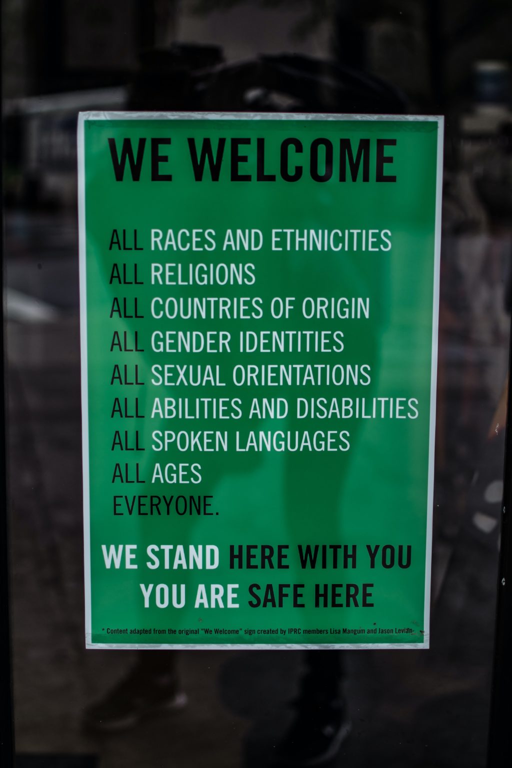Green sign on a window reads "We welcome all races and ethnicities, all religions, all countries of origin, all gender identities, all sexual orientations, all abilities and disabilities, all spoken languages, all ages, everyone. We stand her with you. You are safe here."
