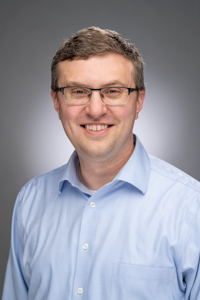 Head shot of Derek Bruff, a light-skinned male who is wearing classes and a light blue button-down shirt.