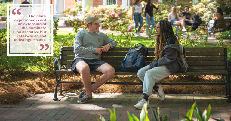 Two young students sit on a bench outside an academic building engaging in conversation. "the Black experience is not an extension of the dominate Elon narrative but interwoven and indistinguishable."