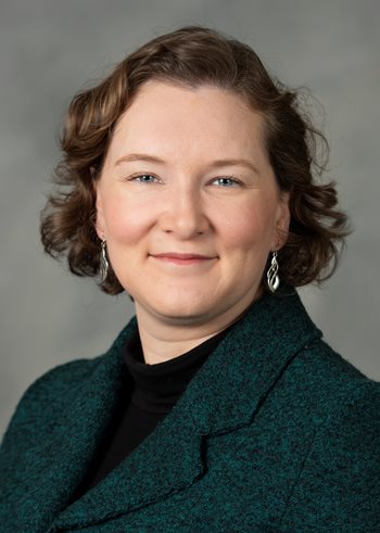 Headshot of a white woman with short brown hair, wearing a black blouse and silver, drop earrings.