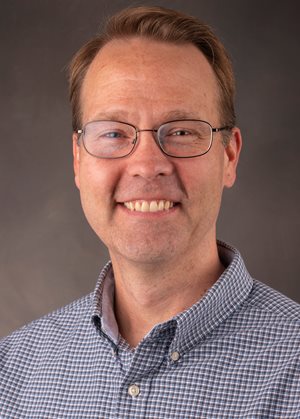 Headshot of white male wearing a checkered blue and white shirt