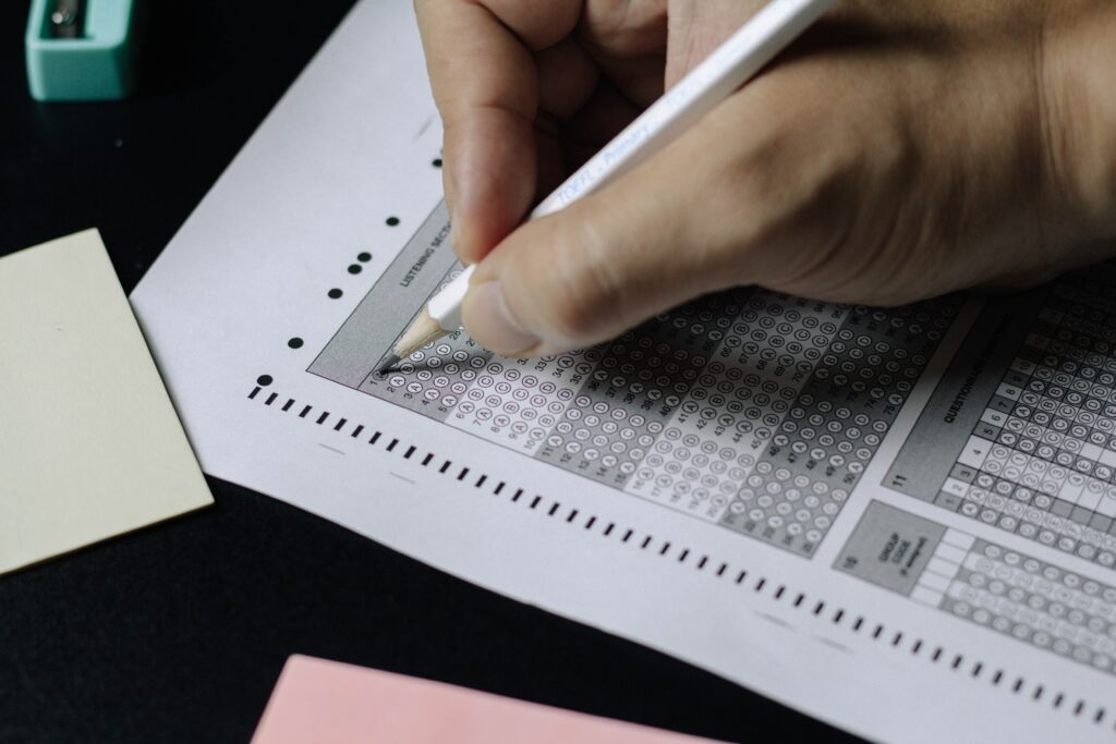 A person's hand holds a pencil above a multiple-choice test bubble sheet.