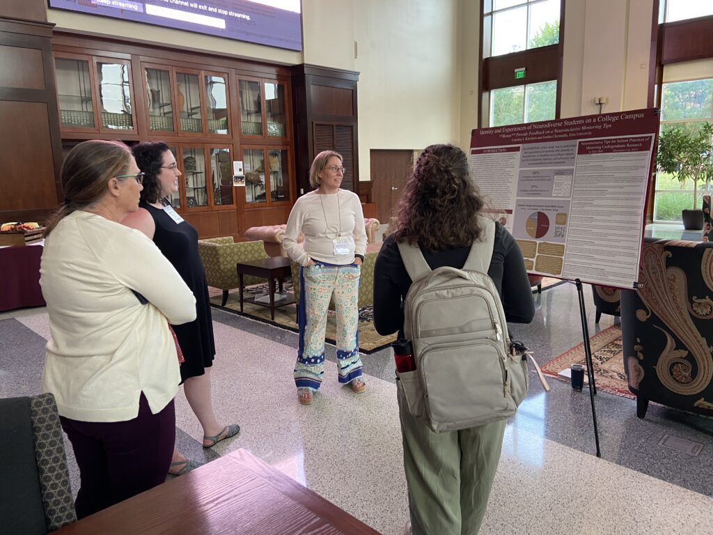 Four people stand in front of an academic conference poster, visiting.