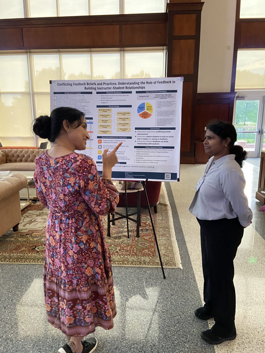Two people stand and talk in front of an academic conference poster.
