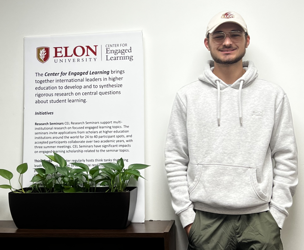 Picture of Nolan Schultheis, standing next to a poster highlighting the Center's initiatives.