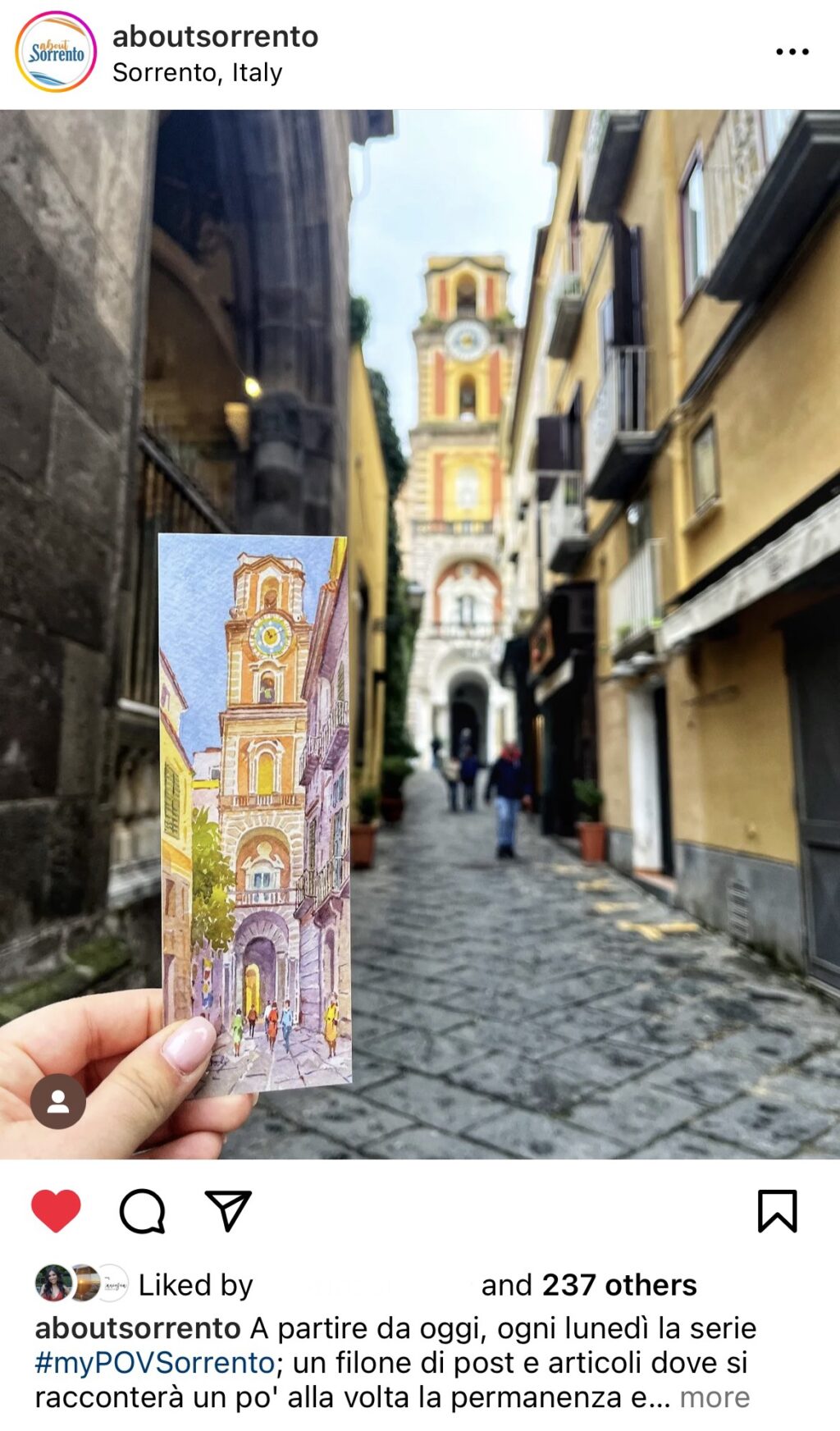 A screenshot of an Instagram post from AboutSorrento shows a narrow city street leading to the bell tower of the Sorrento Cathedral. A hand holds up a small painting of the same view.