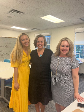 Three women stand together in a classroom