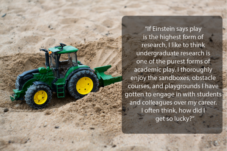 A toy construction vehicle in a sandbox. Text overlay reads, "If Einstein says play is the highest form of research, I like to think undergraduate research is one of the purist forms of academic play. I thoroughly enjoy the sandboxes, obstacle courses and playgrounds I have gotten to engage in with students and colleagues over my career. I often think, how did I get so lucky?"