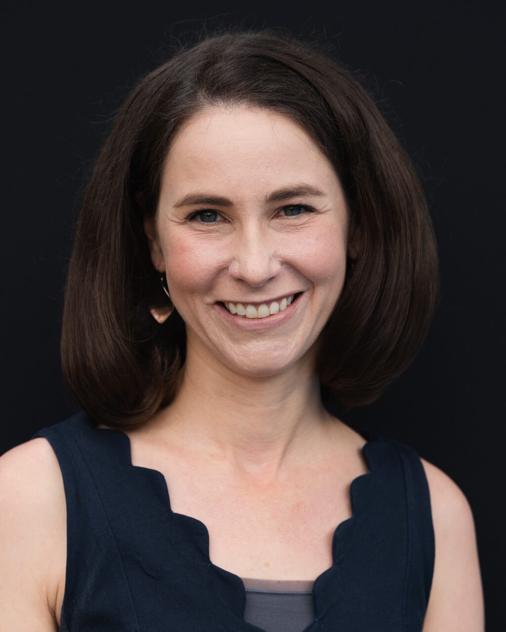 White woman with brown hair just above shoulders and blue eyes smiling.