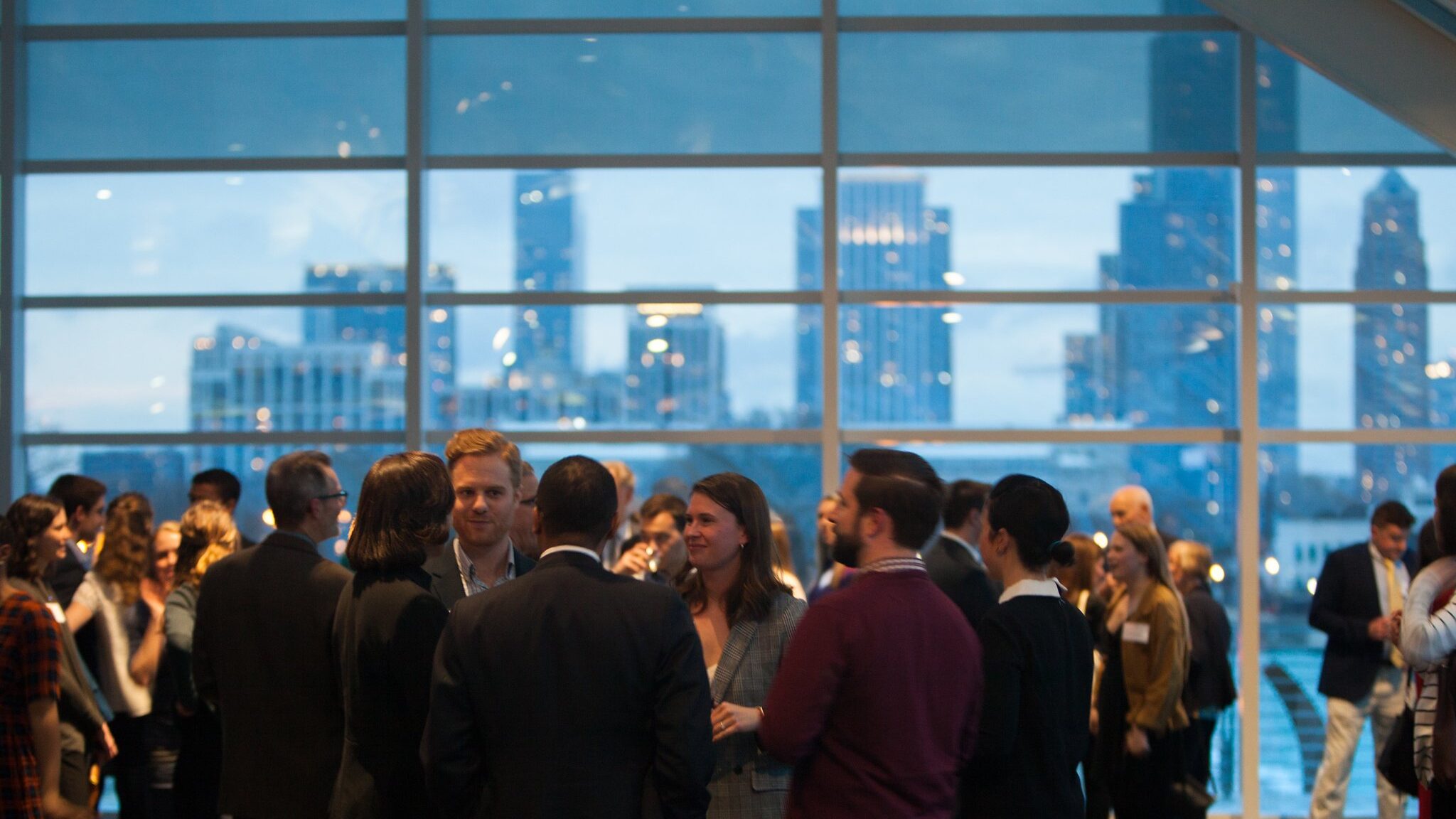 30 people or more gathered in a professional networking space with light blue city skyline in the background.