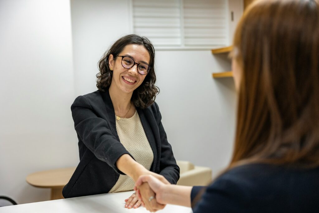 Young woman with brown hair and glasses shaking hands with someone.