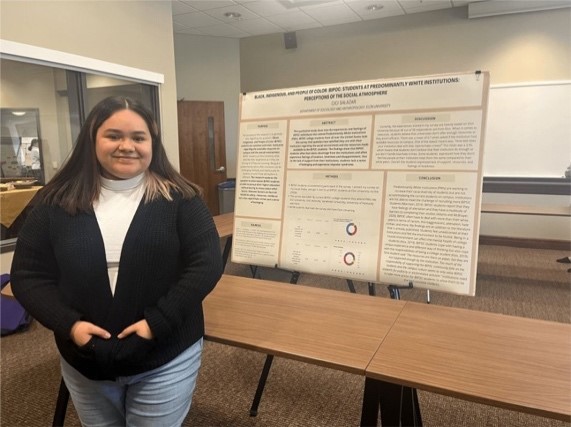 student standing in front of a poster board displaying research
