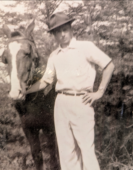 Black and white photo of a man wearing a brimmed hat and standing next to a horse.