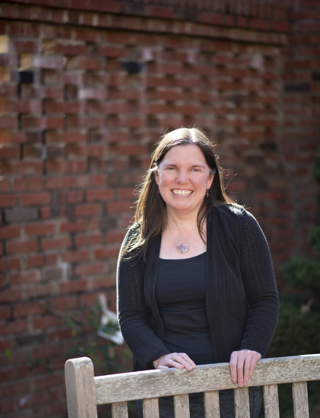 Photo of Jessie Moore standing behind a bunch in a meditation garden, with a brick wall in the background.
