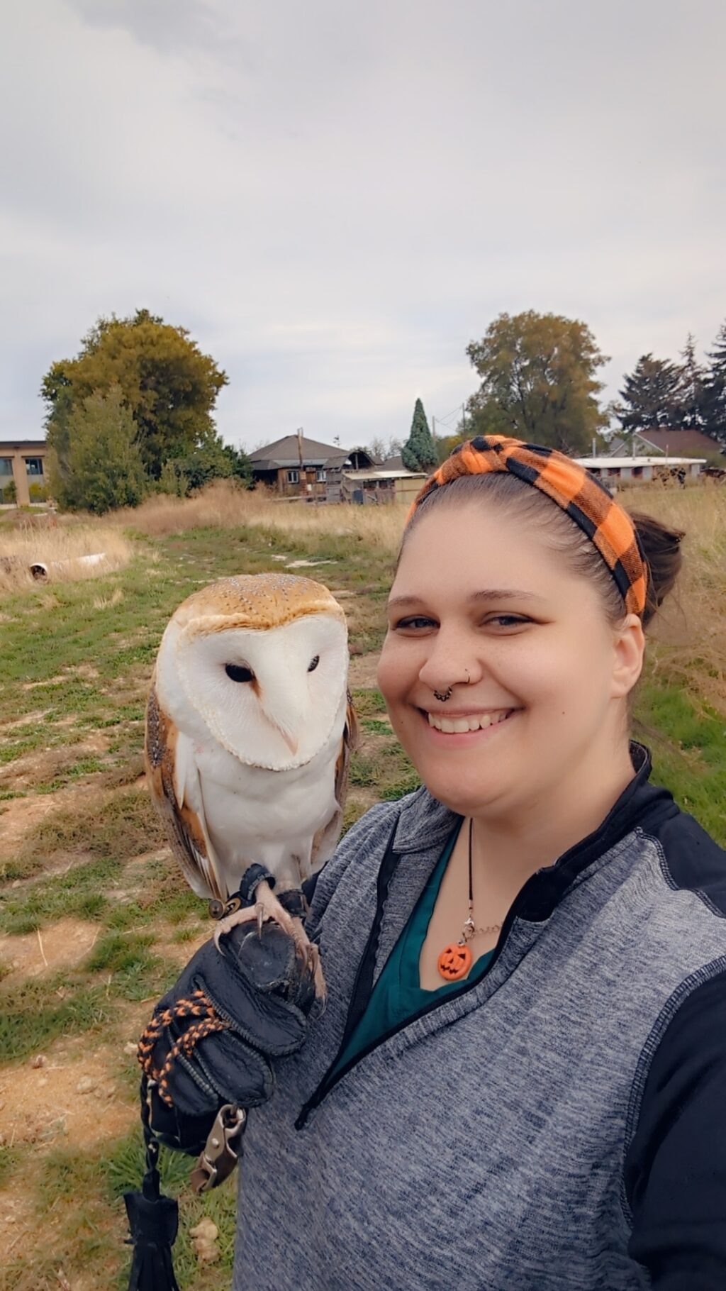 Kasey Wozniak standing in a field with an owl perched on her arm.