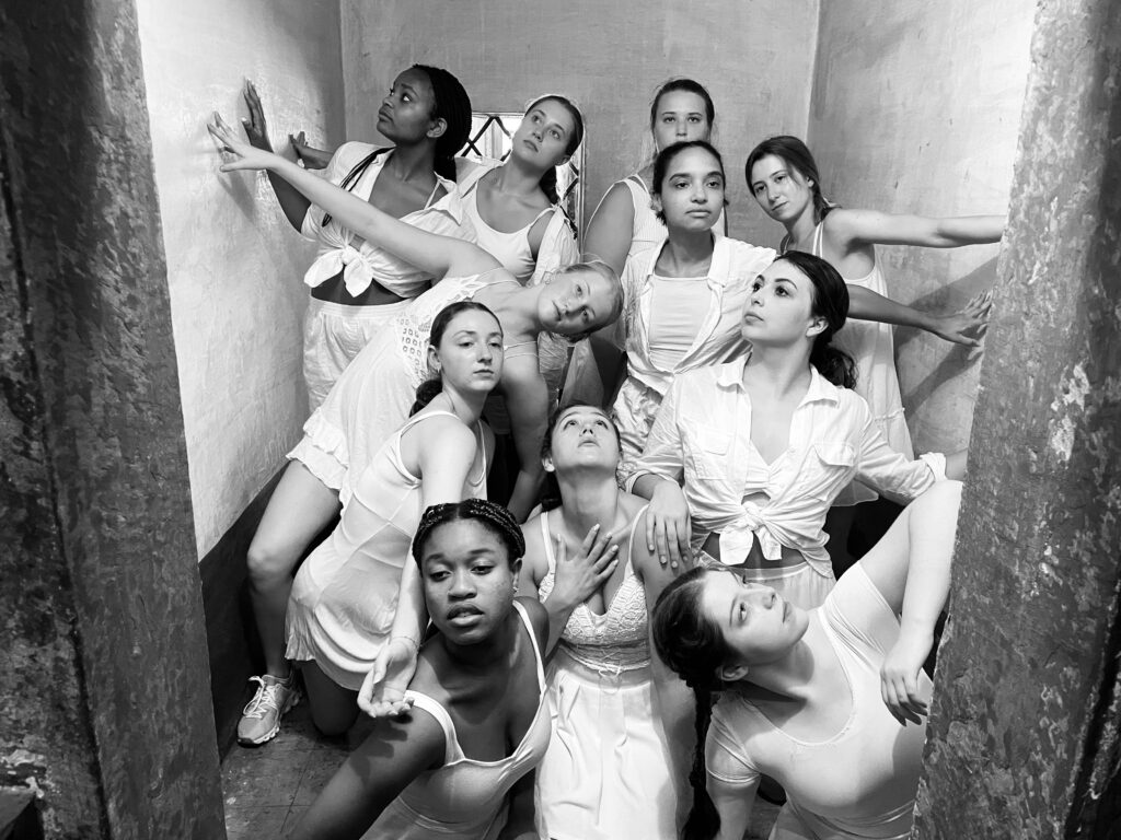 Eleven student dancers in rustic location interacting with walls, each facing different directions