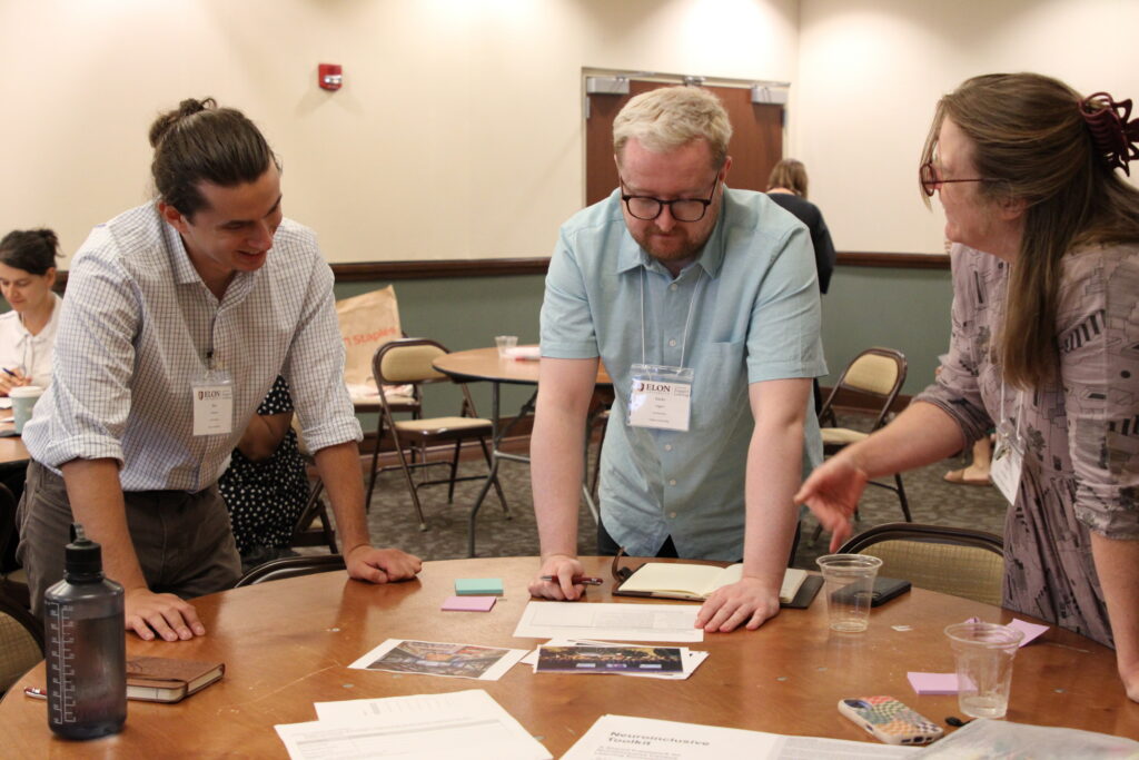 Three conference participants standing around piece of paper at table, discussing.