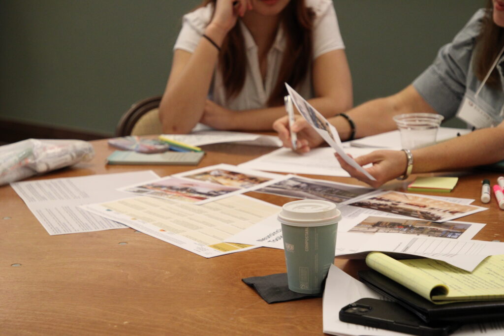 Paper materials scattered across table with people picking them up and pointing.