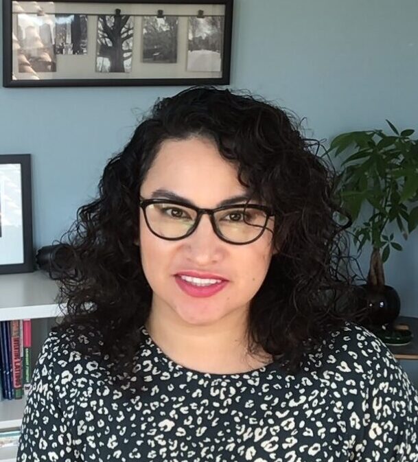 Chicana woman with black wavy hair and glasses in an office